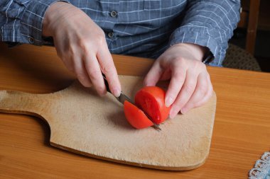 Kırmızı olgun bir domatesi dilimliyorum. Yaşlı bir kadının elleri mutfaktaki bir masayı dilimlemek için domates tutuyor. Yakın plan planı.