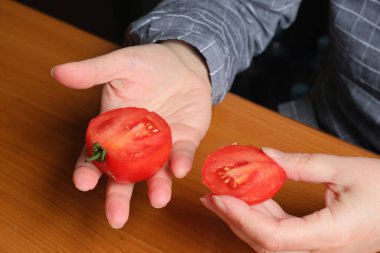 Kırmızı olgun bir domatesi dilimliyorum. Yaşlı bir kadının elleri mutfaktaki bir masayı dilimlemek için domates tutuyor. Yakın plan planı.