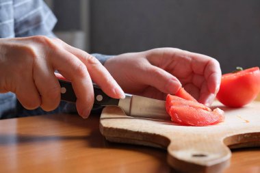 Kırmızı olgun bir domatesi dilimliyorum. Yaşlı bir kadının elleri mutfaktaki bir masayı dilimlemek için domates tutuyor. Yakın plan planı.