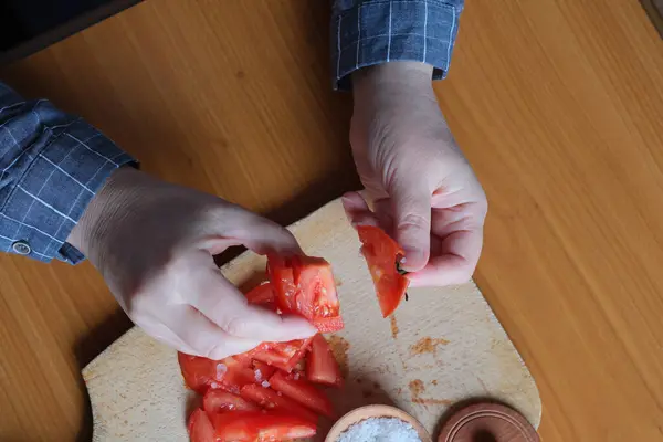 Slicing a red ripe tomato. An elderly woman\'s hands hold a tomato for slicing on a table in the kitchen. Close-up plan.