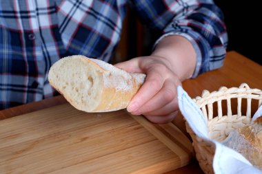 Kahverengi bir masada, mutfakta dilimlenmiş ekmek ekmeği tutan yaşlı bir kadının elleri. Yüzü yok, yakın plan.