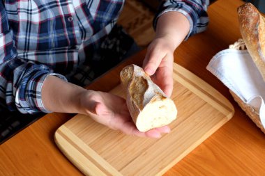 Kahverengi bir masada, mutfakta dilimlenmiş ekmek ekmeği tutan yaşlı bir kadının elleri. Yüzü yok, yakın plan.