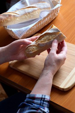 Kahverengi bir masada, mutfakta dilimlenmiş ekmek ekmeği tutan yaşlı bir kadının elleri. Yüzü yok, yakın plan.