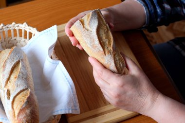 Kahverengi bir masada, mutfakta dilimlenmiş ekmek ekmeği tutan yaşlı bir kadının elleri. Yüzü yok, yakın plan.