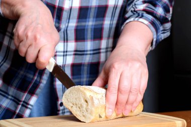 Yaşlı bir kadının elleri, kahverengi bir masanın mutfağında yüzsüz bir bıçakla beyaz buğday ekmeği kesiyor.