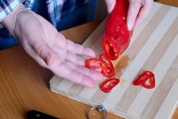 一位老妇人的手砍下红辣椒 放在厨房的一张褐色桌子上 没有脸 而且是特写 — 图库照片