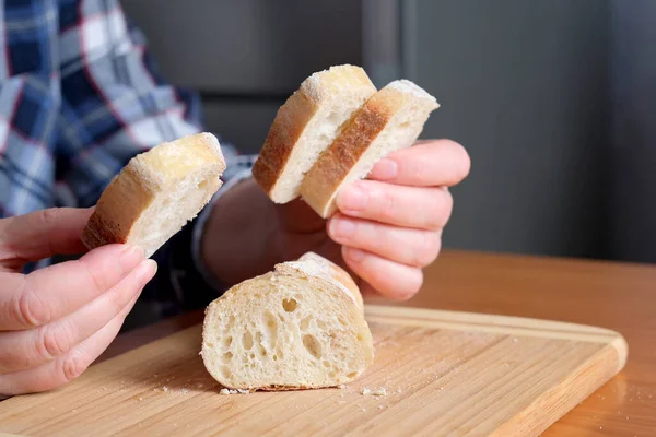 一位老妇人的手 手里拿着切片白麦片面包 放在厨房的一张褐色桌子旁 没有脸 — 图库照片
