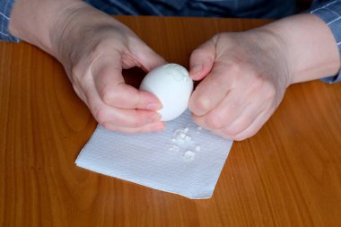 Yaşlı bir kadının elleri kaynamış bir yumurta gösteriyor ve kahverengi bir masadaki mutfakta soyuyorlar, yüzü yok, yakın plan.