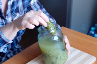 Yaşlı bir kadının elleri, bir kavanozdan lezzetli ev yapımı salatalık turşusunu çıkarır. Kahverengi bir masada çerez niyetine, yüzü olmadan, yakın çekim yapmak için.