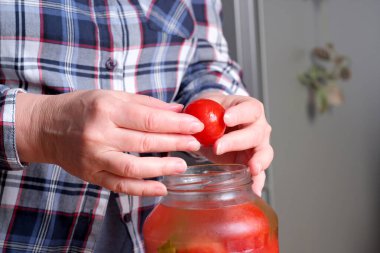 Yaşlı bir kadının elleri, kahverengi bir masadaki kavanozdan lezzetli ev yapımı domatesleri yüzsüz, yakın plan çekimleri ile çıkarıyor.