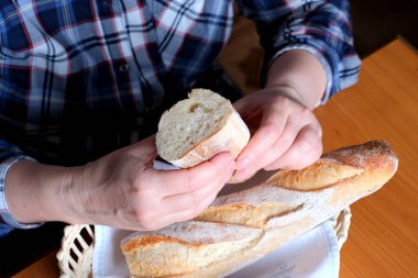Kahverengi bir masada, mutfakta dilimlenmiş ekmek ekmeği tutan yaşlı bir kadının elleri. Yüzü yok, yakın plan.
