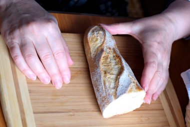Kahverengi bir masada, mutfakta dilimlenmiş ekmek ekmeği tutan yaşlı bir kadının elleri. Yüzü yok, yakın plan.