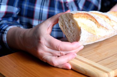 Kahverengi bir masada, mutfakta dilimlenmiş ekmek ekmeği tutan yaşlı bir kadının elleri. Yüzü yok, yakın plan.