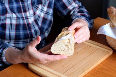 Kahverengi bir masada, mutfakta dilimlenmiş ekmek ekmeği tutan yaşlı bir kadının elleri. Yüzü yok, yakın plan.