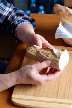 Kahverengi bir masada, mutfakta dilimlenmiş ekmek ekmeği tutan yaşlı bir kadının elleri. Yüzü yok, yakın plan.