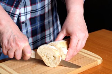 Yaşlı bir kadının elleri, kahverengi bir masanın mutfağında yüzsüz bir bıçakla beyaz buğday ekmeği kesiyor.