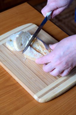 Yaşlı bir kadının elleri, kahverengi bir masanın mutfağında yüzsüz bir bıçakla beyaz buğday ekmeği kesiyor.