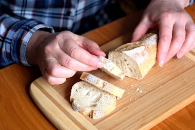Kahverengi bir masada, mutfakta dilimlenmiş ekmek ekmeği tutan yaşlı bir kadının elleri. Yüzü yok, yakın plan.