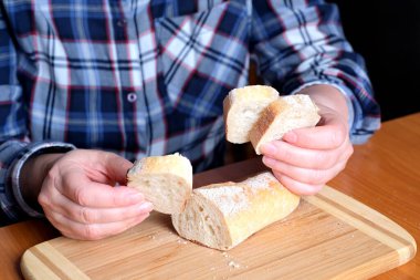 Kahverengi bir masada, mutfakta dilimlenmiş ekmek ekmeği tutan yaşlı bir kadının elleri. Yüzü yok, yakın plan.