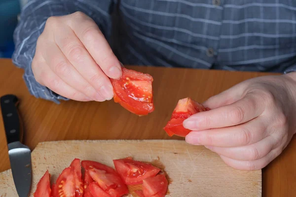 一位老妇人的手在厨房里切一个红熟的西红柿 放在一块切菜板上 放在一张褐色的桌子上 没有脸 是特写 — 图库照片