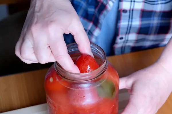 一位老妇人的手从厨房里一个褐色桌子旁的罐子里取出美味的自制腌制西红柿 没有脸 而且是特写 — 图库照片