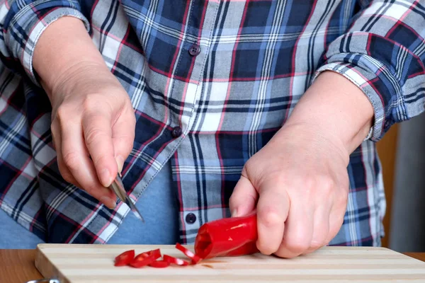 一位老妇人的手砍下红辣椒 放在厨房的一张褐色桌子上 没有脸 而且是特写 — 图库照片