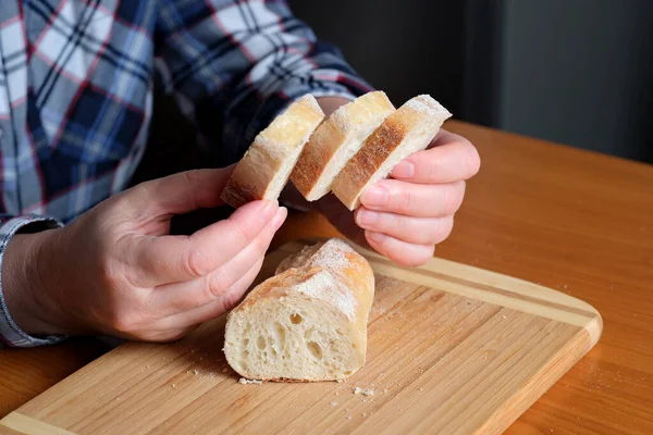 Kahverengi bir masada, mutfakta dilimlenmiş ekmek ekmeği tutan yaşlı bir kadının elleri. Yüzü yok, yakın plan.
