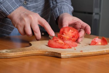 Yaşlı bir kadının elleri kesme tahtasıyla kırmızı olgun bir domatesi kesiyor kahverengi bir masada atıştırmak için, yüzü yok, yakın plan.