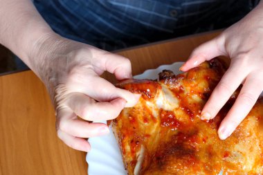 Yaşlı bir kadının elleri ızgara bir tavuğu çalıştırıyor ve kahverengi bir masada, yüzü olmadan, yakın plan çekimde sergiliyor.
