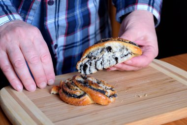 Yaşlı bir kadının elleri, mutfaktaki haşhaş tohumlu tatlı bir çöreği yüzsüz, yakın planda, kahverengi bir masada çalıştırıyor.