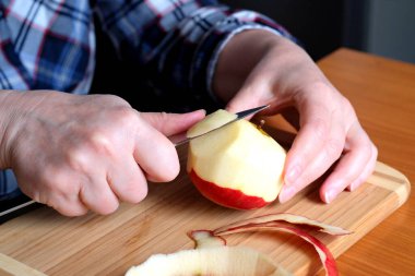 Yaşlı bir kadının elleri, kırmızı, sulu, sulu bir elmayı yüzsüz, kahverengi bir masadaki bıçakla soyar.