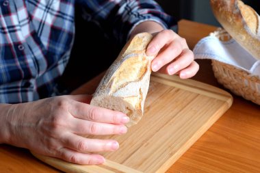 Kahverengi bir masada, mutfakta dilimlenmiş ekmek ekmeği tutan yaşlı bir kadının elleri. Yüzü yok, yakın plan.