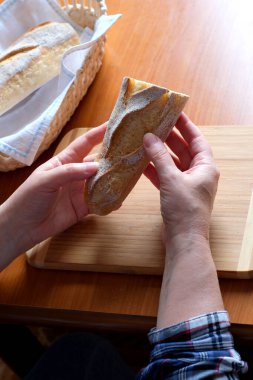 Kahverengi bir masada, mutfakta dilimlenmiş ekmek ekmeği tutan yaşlı bir kadının elleri. Yüzü yok, yakın plan.