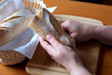 Kahverengi bir masada, mutfakta dilimlenmiş ekmek ekmeği tutan yaşlı bir kadının elleri. Yüzü yok, yakın plan.