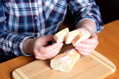 Kahverengi bir masada, mutfakta dilimlenmiş ekmek ekmeği tutan yaşlı bir kadının elleri. Yüzü yok, yakın plan.
