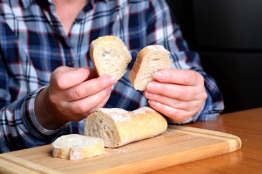 Kahverengi bir masada, mutfakta dilimlenmiş ekmek ekmeği tutan yaşlı bir kadının elleri. Yüzü yok, yakın plan.