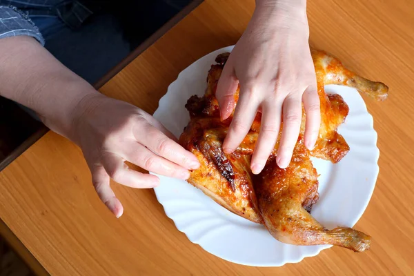 The hands of an elderly woman operate a grilled chicken and display it in the kitchen at a brown table, without a face, close-up