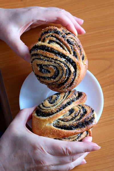 The hands of an elderly woman operate a sweet bun with poppy seeds in the kitchen at a brown table, without a face, close-up