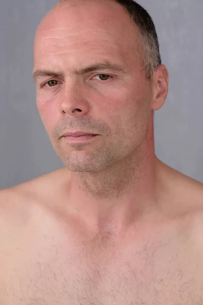 A young man with a short haircut with a naked torso on a gray background, close-up.