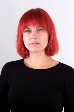 Kısa turuncu saçlı, siyah tişörtlü ve kot pantolonlu, beyaz arka planda stüdyoda poz veren çekici bir kadın..