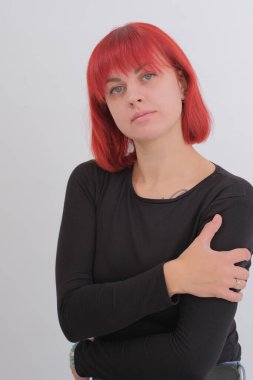 Kısa turuncu saçlı, siyah tişörtlü ve kot pantolonlu, beyaz arka planda stüdyoda poz veren çekici bir kadın..