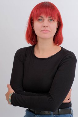 Kısa turuncu saçlı, siyah tişörtlü ve kot pantolonlu, beyaz arka planda stüdyoda poz veren çekici bir kadın..