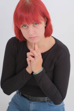 Kısa turuncu saçlı, siyah tişörtlü ve kot pantolonlu, beyaz arka planda stüdyoda poz veren çekici bir kadın..