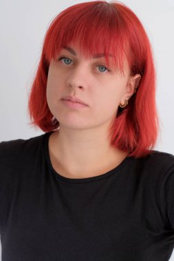 Kısa turuncu saçlı, siyah tişörtlü ve kot pantolonlu, beyaz arka planda stüdyoda poz veren çekici bir kadın..