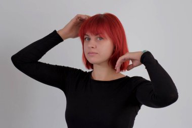 Kısa turuncu saçlı, siyah tişörtlü ve kot pantolonlu, beyaz arka planda stüdyoda poz veren çekici bir kadın..