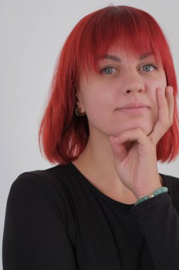 Kısa turuncu saçlı, siyah tişörtlü ve kot pantolonlu, beyaz arka planda stüdyoda poz veren çekici bir kadın..