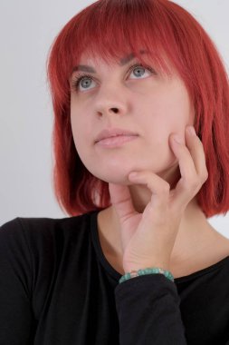 Kısa turuncu saçlı, siyah tişörtlü ve kot pantolonlu, beyaz arka planda stüdyoda poz veren çekici bir kadın..