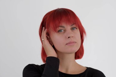 Kısa turuncu saçlı, siyah tişörtlü ve kot pantolonlu, beyaz arka planda stüdyoda poz veren çekici bir kadın..