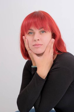 Kısa turuncu saçlı, siyah tişörtlü ve kot pantolonlu, beyaz arka planda stüdyoda poz veren çekici bir kadın..