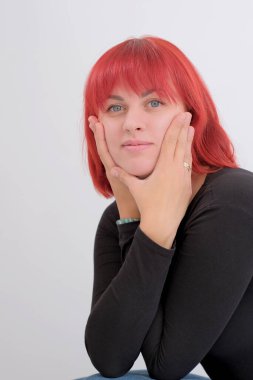 Kısa turuncu saçlı, siyah tişörtlü ve kot pantolonlu, beyaz arka planda stüdyoda poz veren çekici bir kadın..